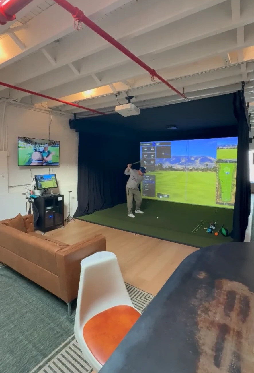 Member mid-swing in the Prospect Heights Trackman iO bay with leather couch and orange chair