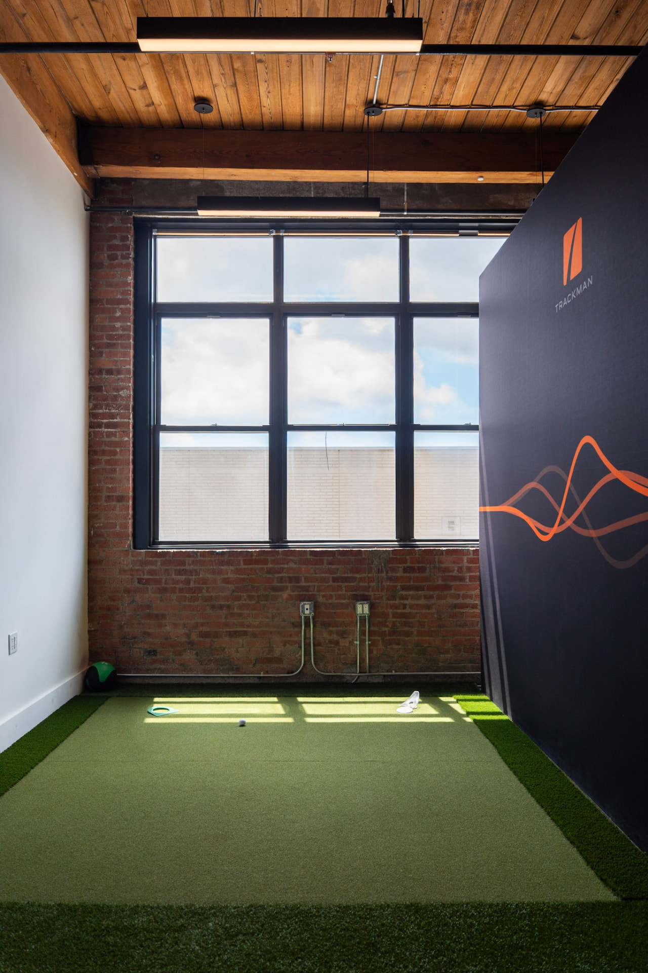 Trackman iO bay interior with turf, brick wall, and tall windows